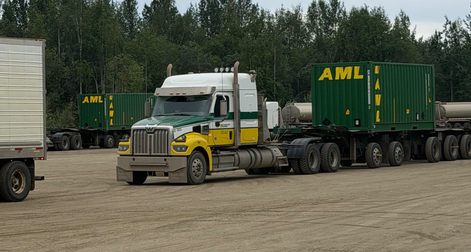 Semi truck and green freight containers staged in a gravel yard.