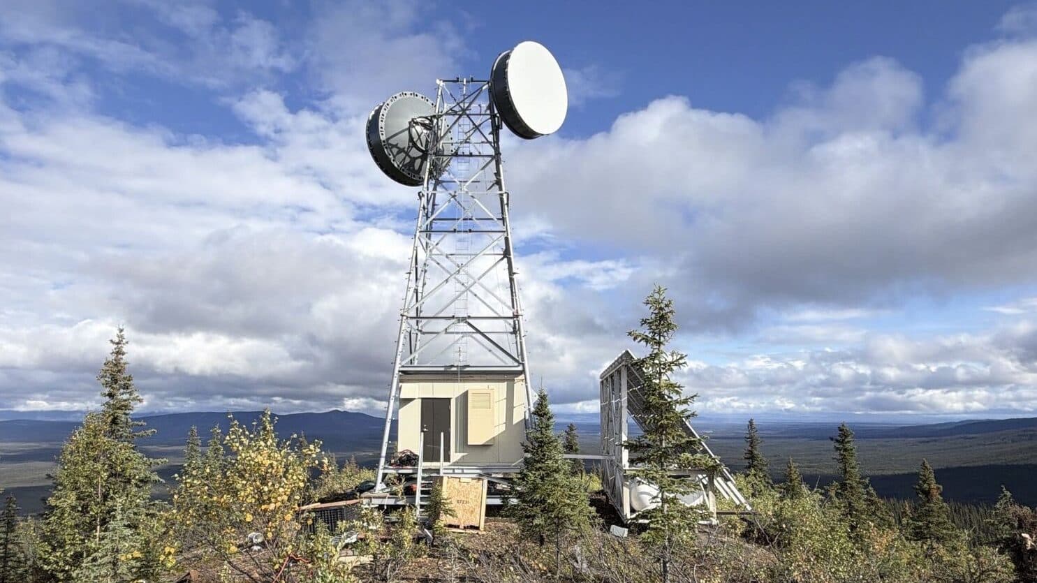 Finished lattice tower with two microwave dishes, an equipment shelter and a solar array on a hilltop.