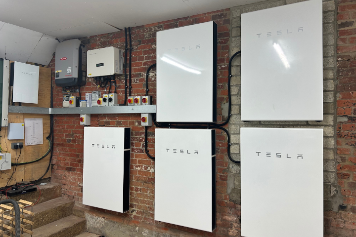 Multiple Tesla Powerwall units installed on a brick wall in a commercial battery storage configuration.